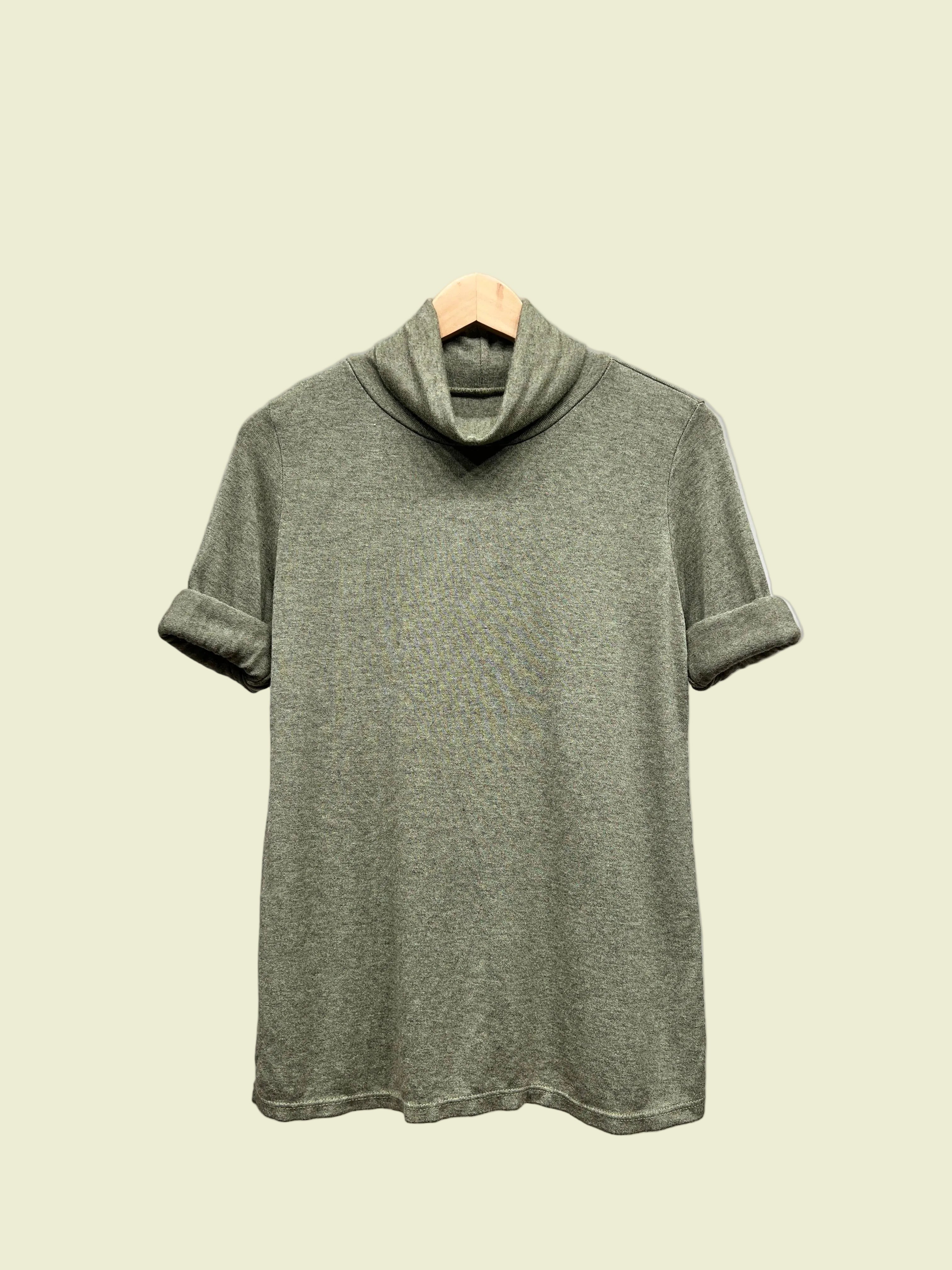 Green turtleneck top on a hanger against a plain background