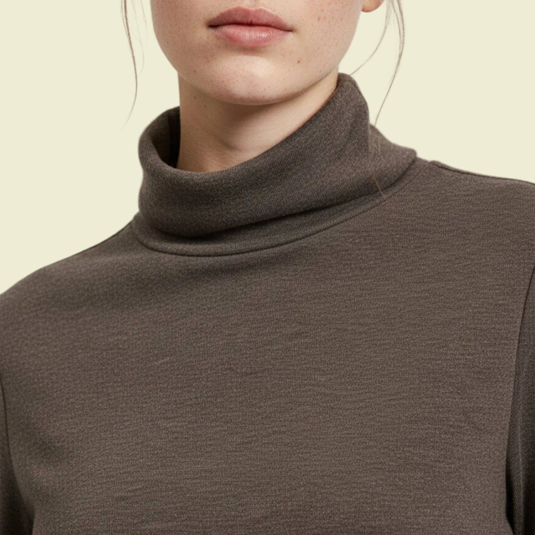 Close-up of a person wearing a brown turtleneck top on a grey background