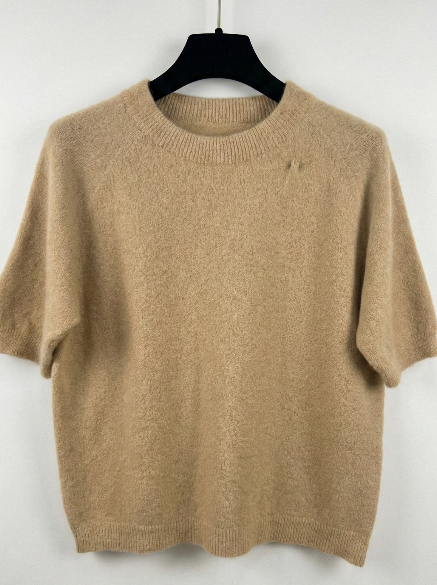 Beige sweater on a black hanger against a white background