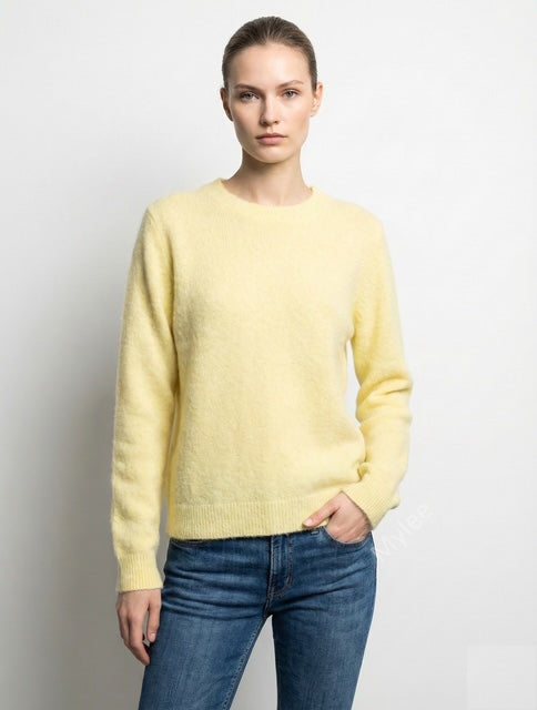 Woman wearing a light yellow sweater and blue jeans against a plain background