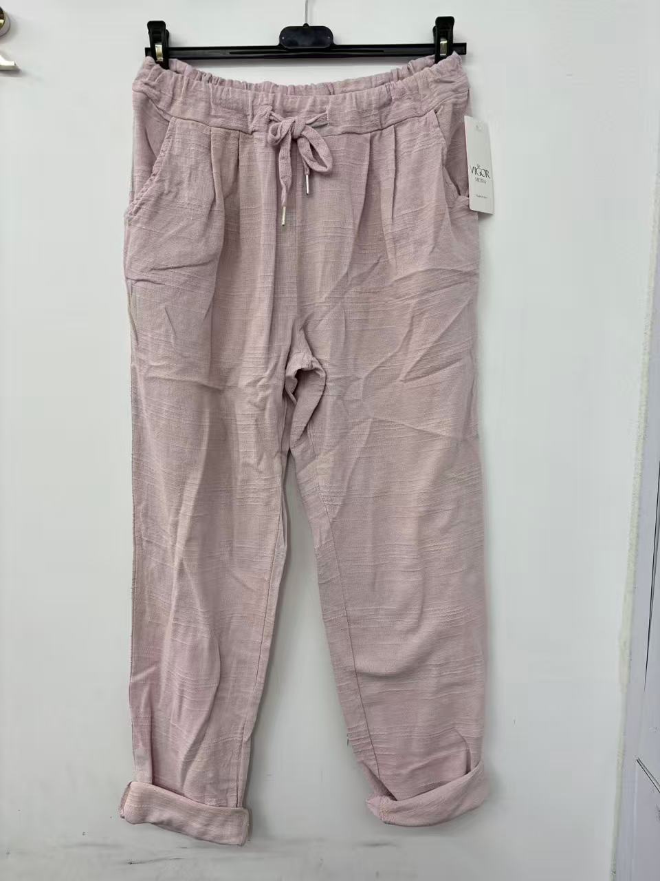 Pink cotton pants on a hanger against a white wall
