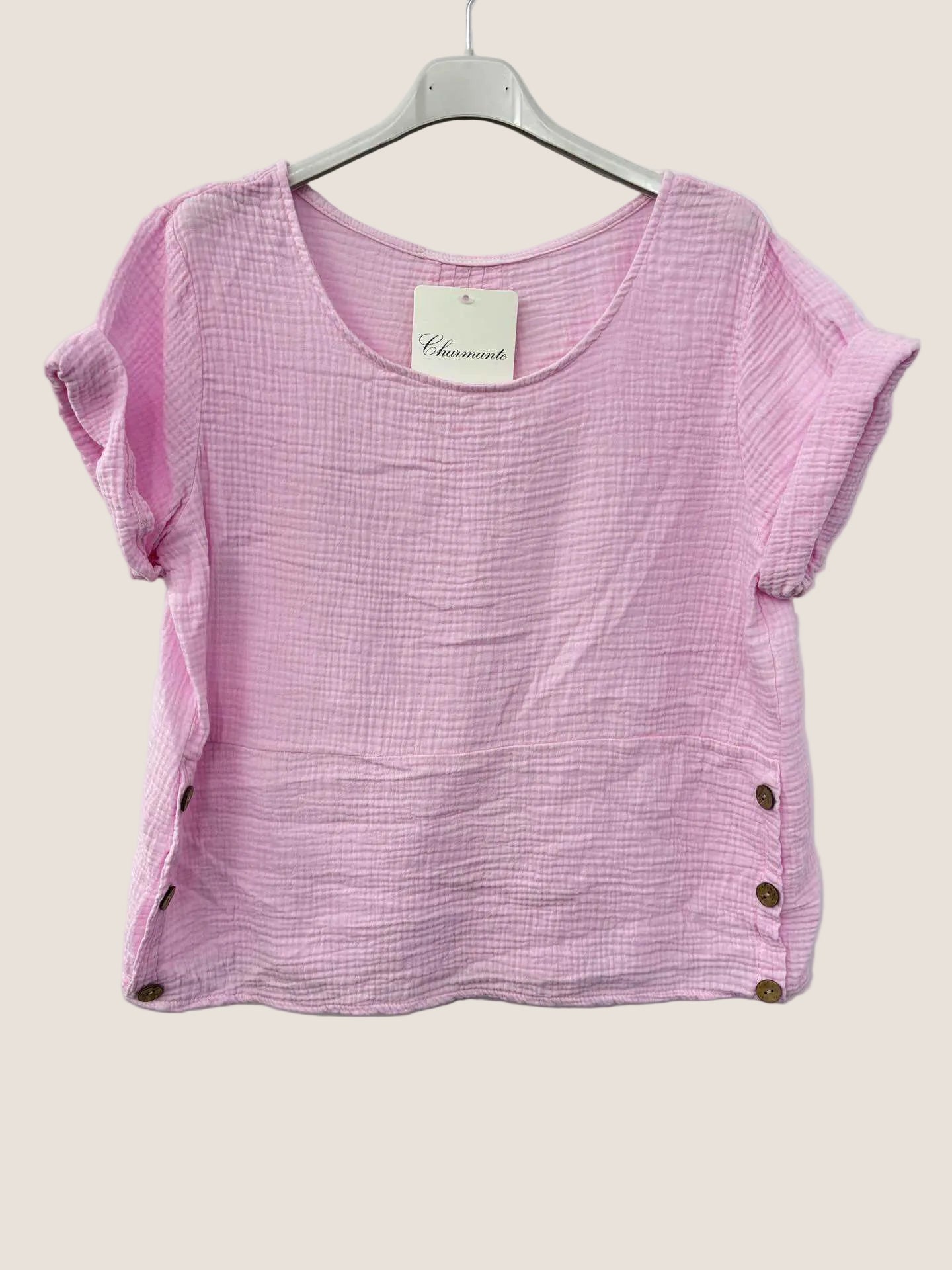 Pink cotton gauze top with buttons on a hanger against a white background