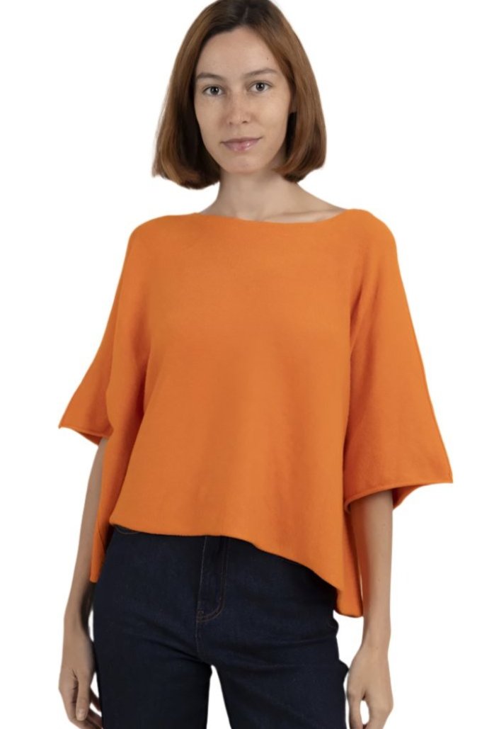 A woman wearing an orange, boxy cropped chunky knit sweater with 3/4 sleeves and a boat neck.