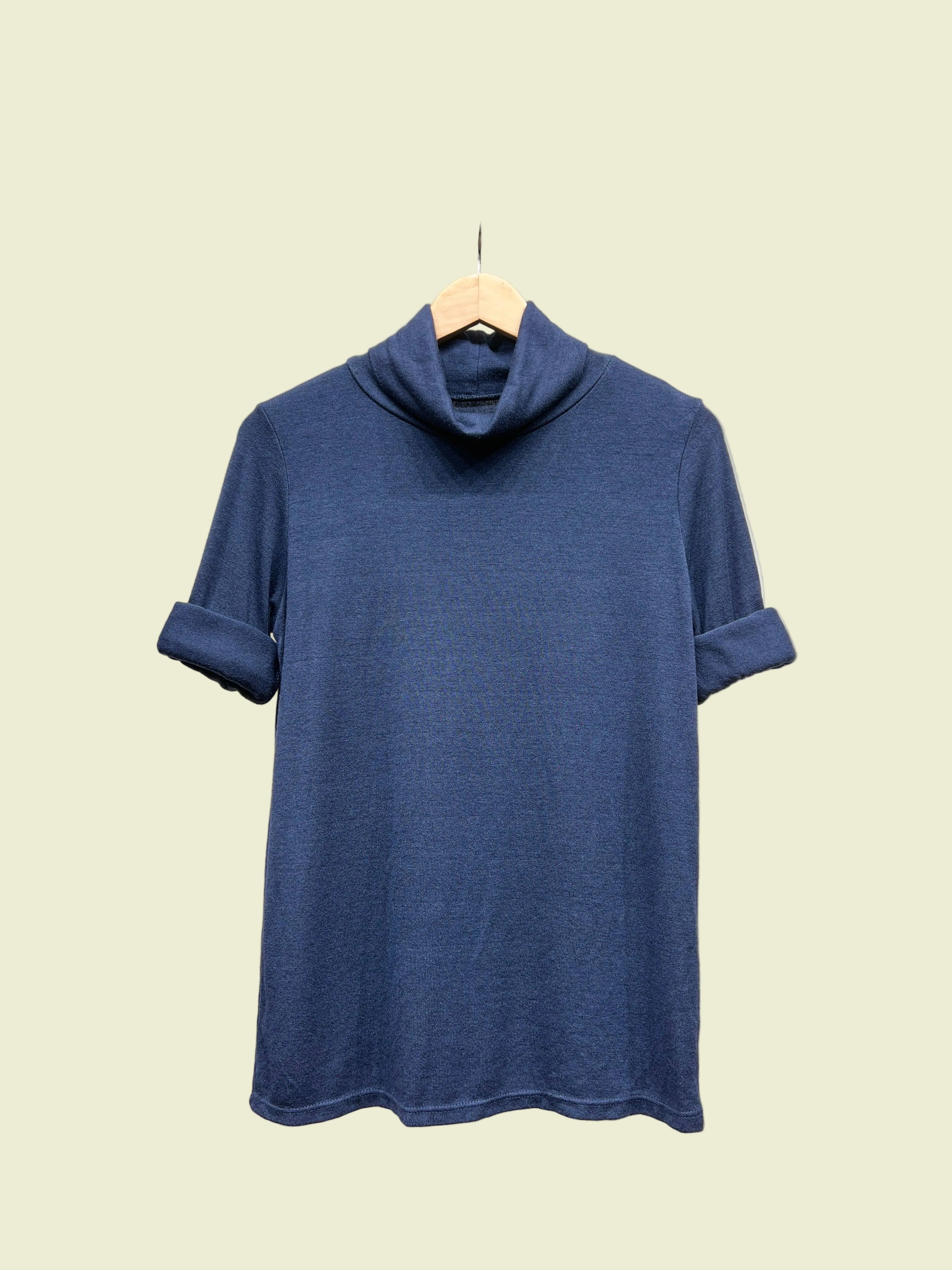 Blue turtleneck top on a hanger against a neutral background