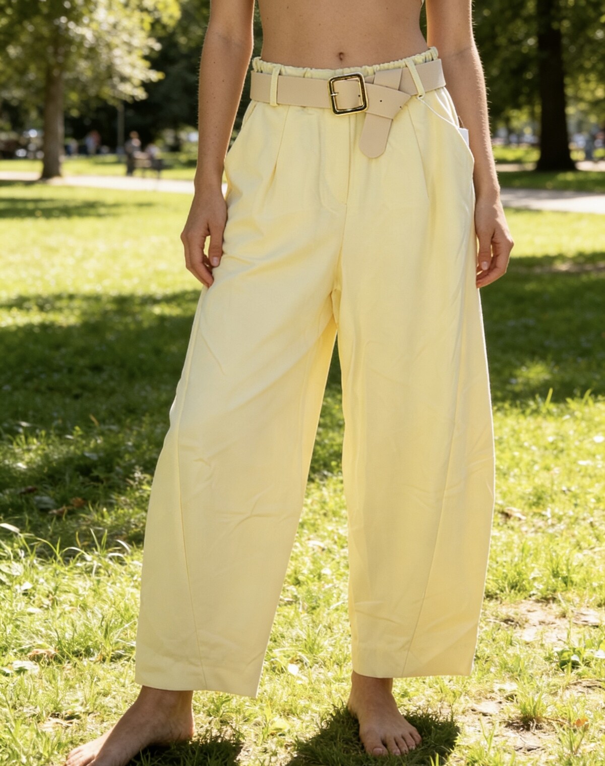 Person wearing light yellow wide-leg pants with a belt in a park setting