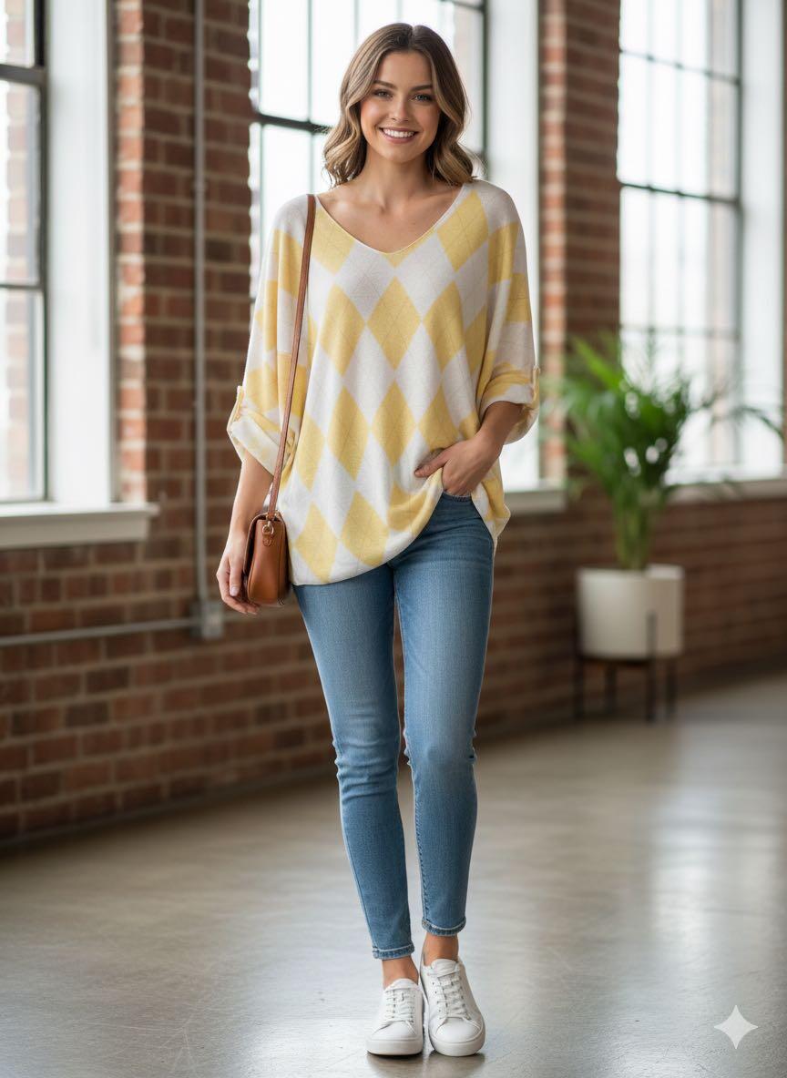 Woman wearing a yellow and white patterned sweater with blue jeans indoors.