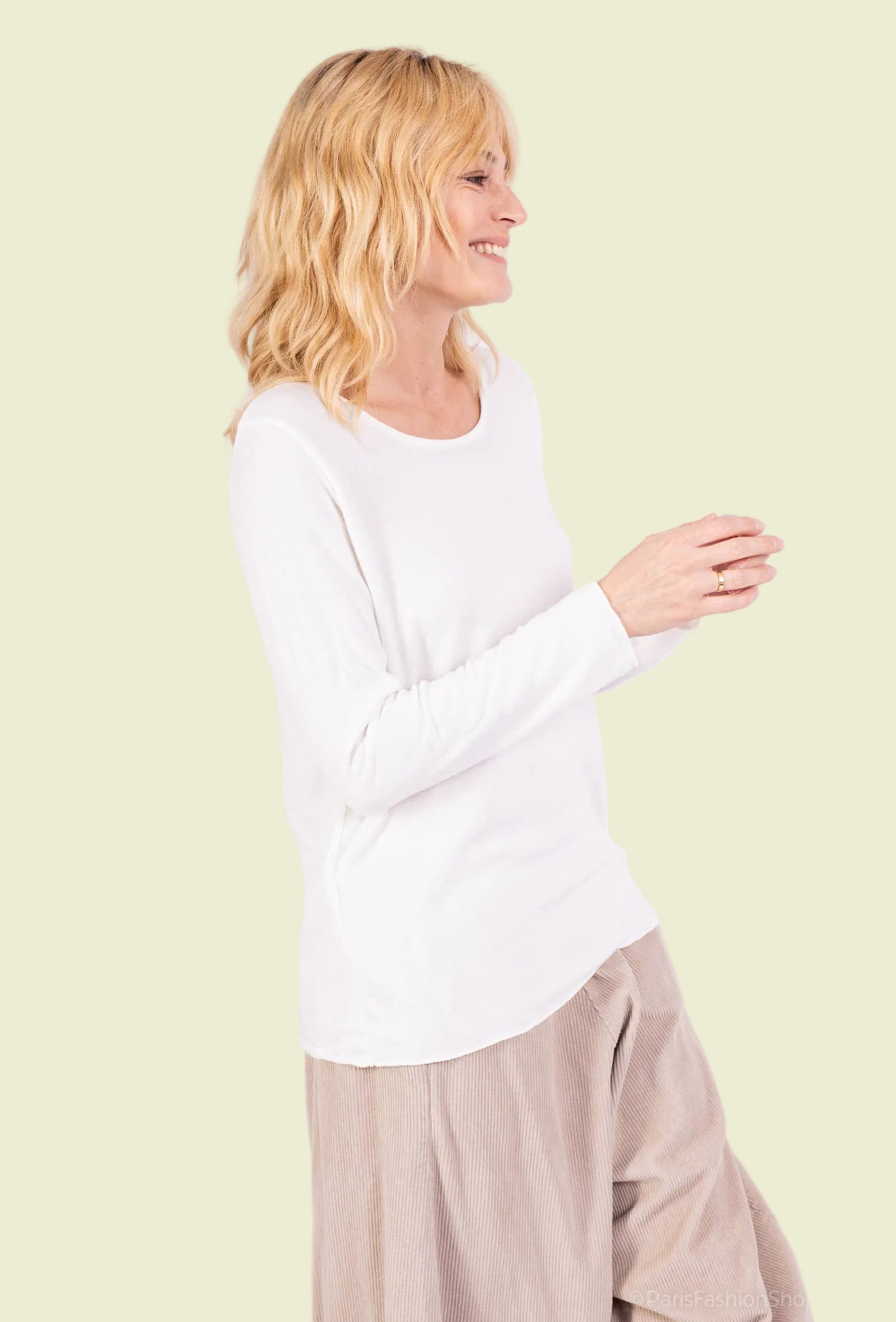 Woman wearing a white long-sleeve top and beige pants on a white background