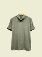 Green turtleneck top on a hanger against a plain background