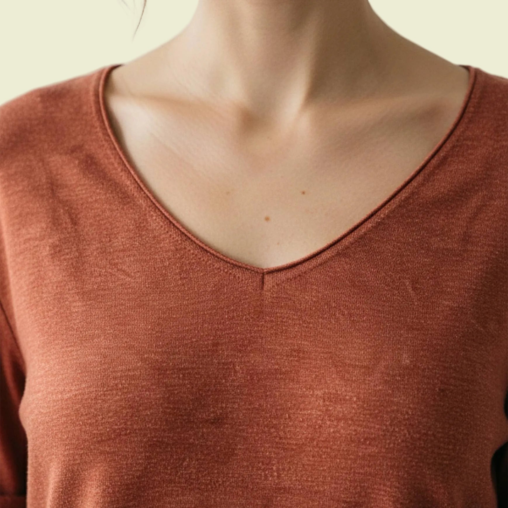 Close-up of a person wearing a rust-colored long-sleeve shirt with a neutral background