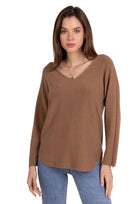 Woman wearing a brown long-sleeve top and blue jeans on a plain background