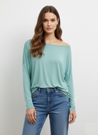 Woman wearing a light blue off-shoulder top and blue jeans on a white background