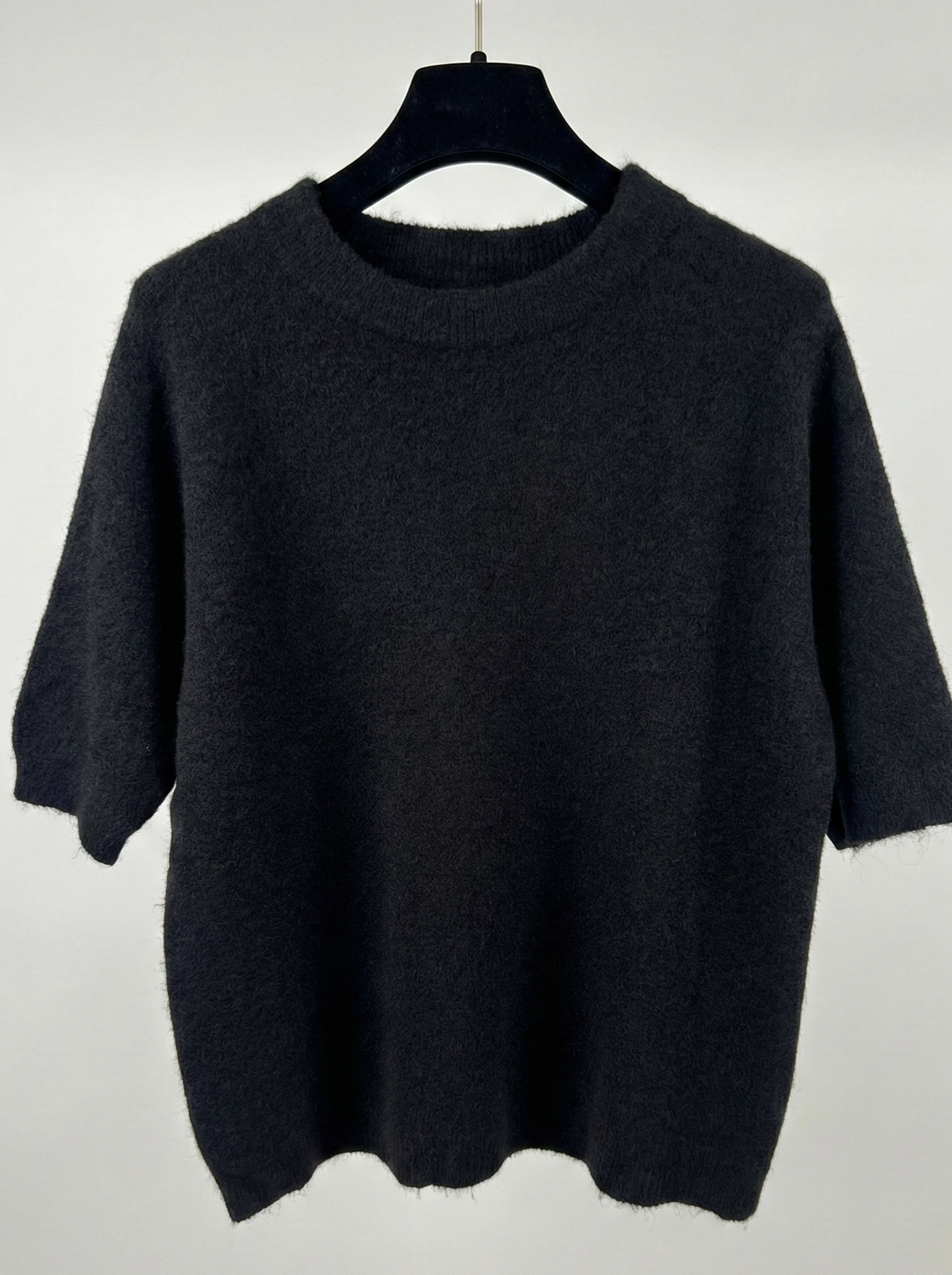 Black sweater on a hanger against a white background