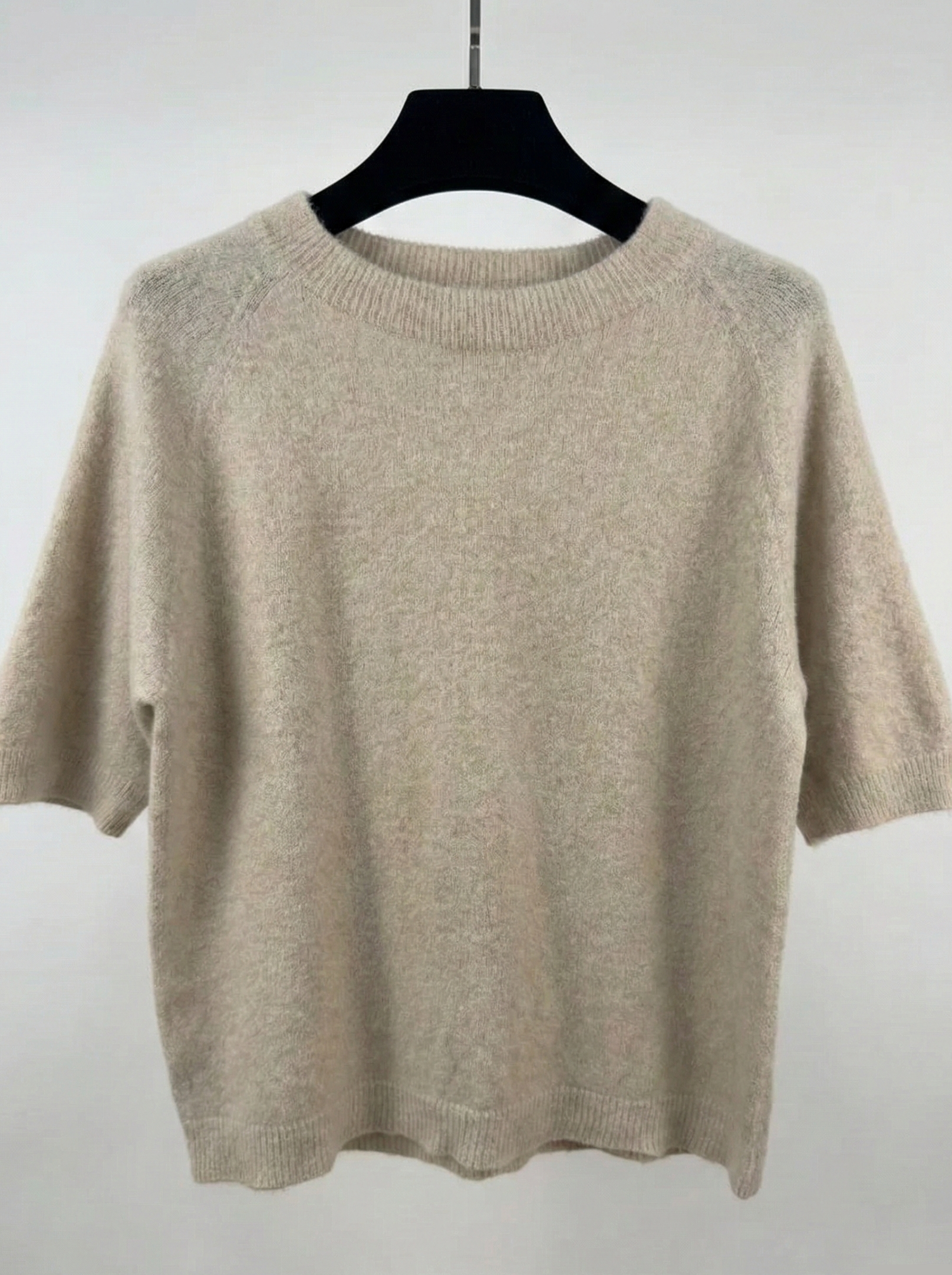 Beige sweater on a black hanger against a white background