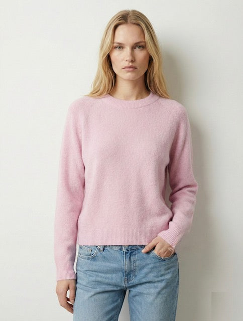 Woman wearing a pink sweater and blue jeans against a plain background