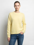 Woman wearing a light yellow sweater and blue jeans against a plain background