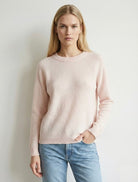 Woman wearing a light pink sweater and blue jeans against a plain background