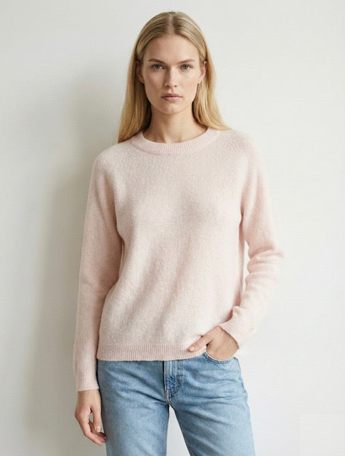 Woman wearing a light pink sweater and blue jeans against a plain background