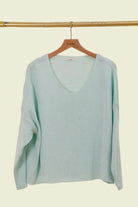 Light blue sweater on a wooden hanger against a beige background
