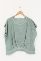 Green sleeveless top on a wooden hanger against a white background