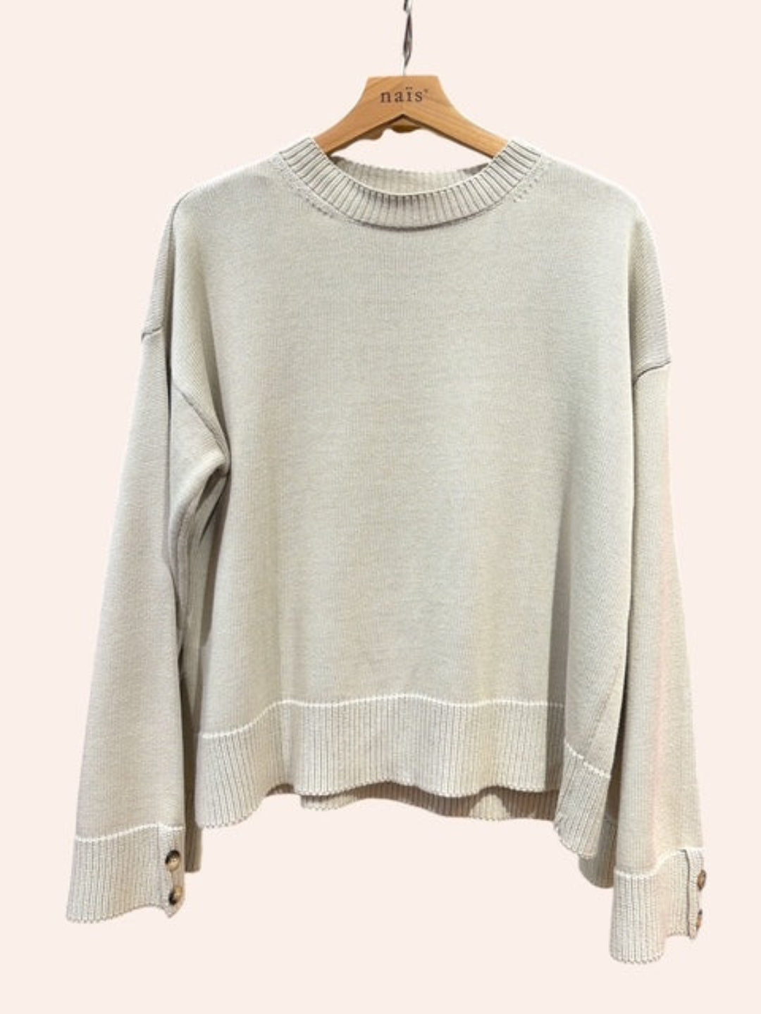 Beige sweater on a hanger against a light pink background