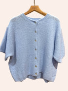 Light blue knitted cardigan on a wooden hanger against a plain background