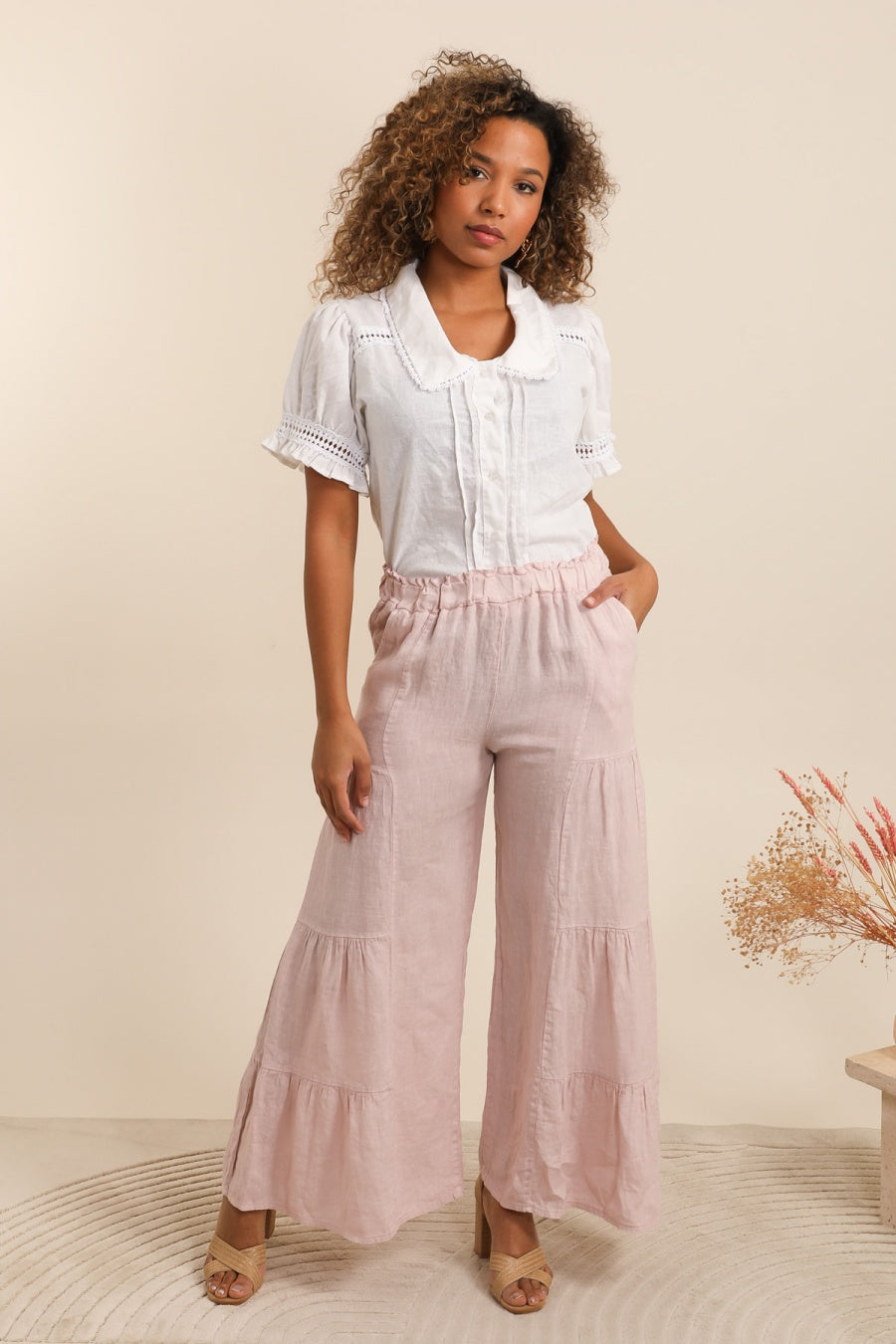 Woman wearing a white blouse and pink tiered pants against a beige background
