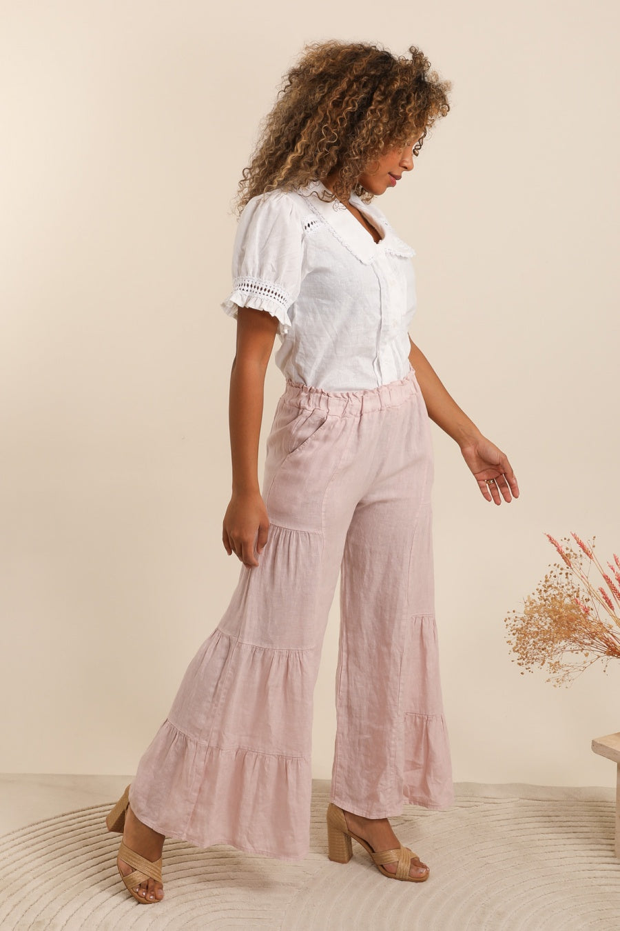 Woman wearing a white blouse and pink tiered pants against a beige background