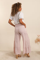 Woman wearing a white top and light pink pants on a beige background