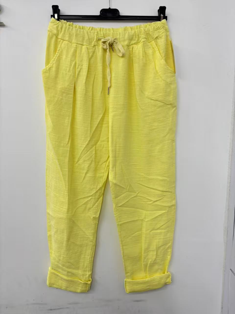 Yellow pants with a drawstring on a hanger against a white background