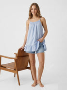 Woman wearing a light blue dress and shorts standing next to a wooden chair on a white background
