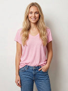 Woman wearing a pink t-shirt and blue jeans against a plain background