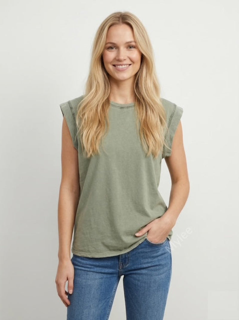 Woman wearing a green sleeveless top and blue jeans on a plain background
