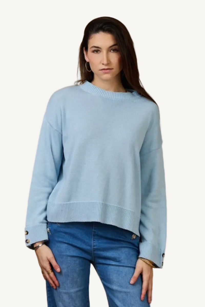 Woman wearing a light blue sweater and blue jeans against a beige background