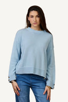 Woman wearing a light blue sweater and blue jeans against a beige background
