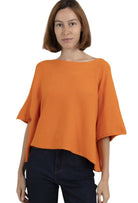 A woman wearing an orange, boxy cropped chunky knit sweater with 3/4 sleeves and a boat neck.
