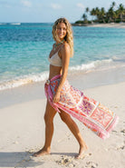 Woman walking on a beach with a colorful sarong wrapped around her waist.