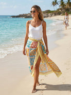 Woman on a beach wearing a white top and colorful sarong
