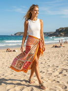 Woman walking on a beach wearing a colorful sarong and white top.