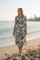 Woman in a floral dress standing on a beach with ocean and sky in the background