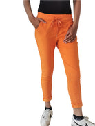 A person standing in an indoor setting wearing orange Magic stretch trousers with an elasticated waist, side pockets, and white sneakers.