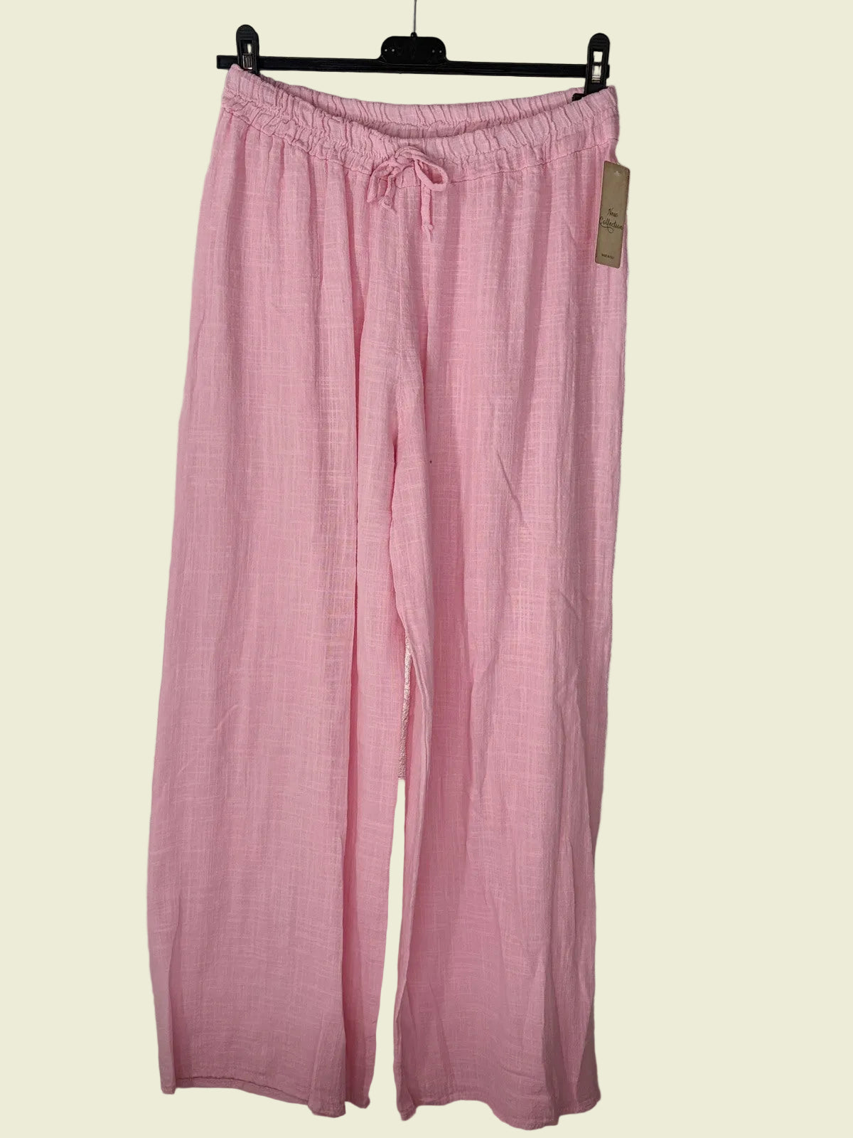 Pink pants hanging on a rack against a textured wall.