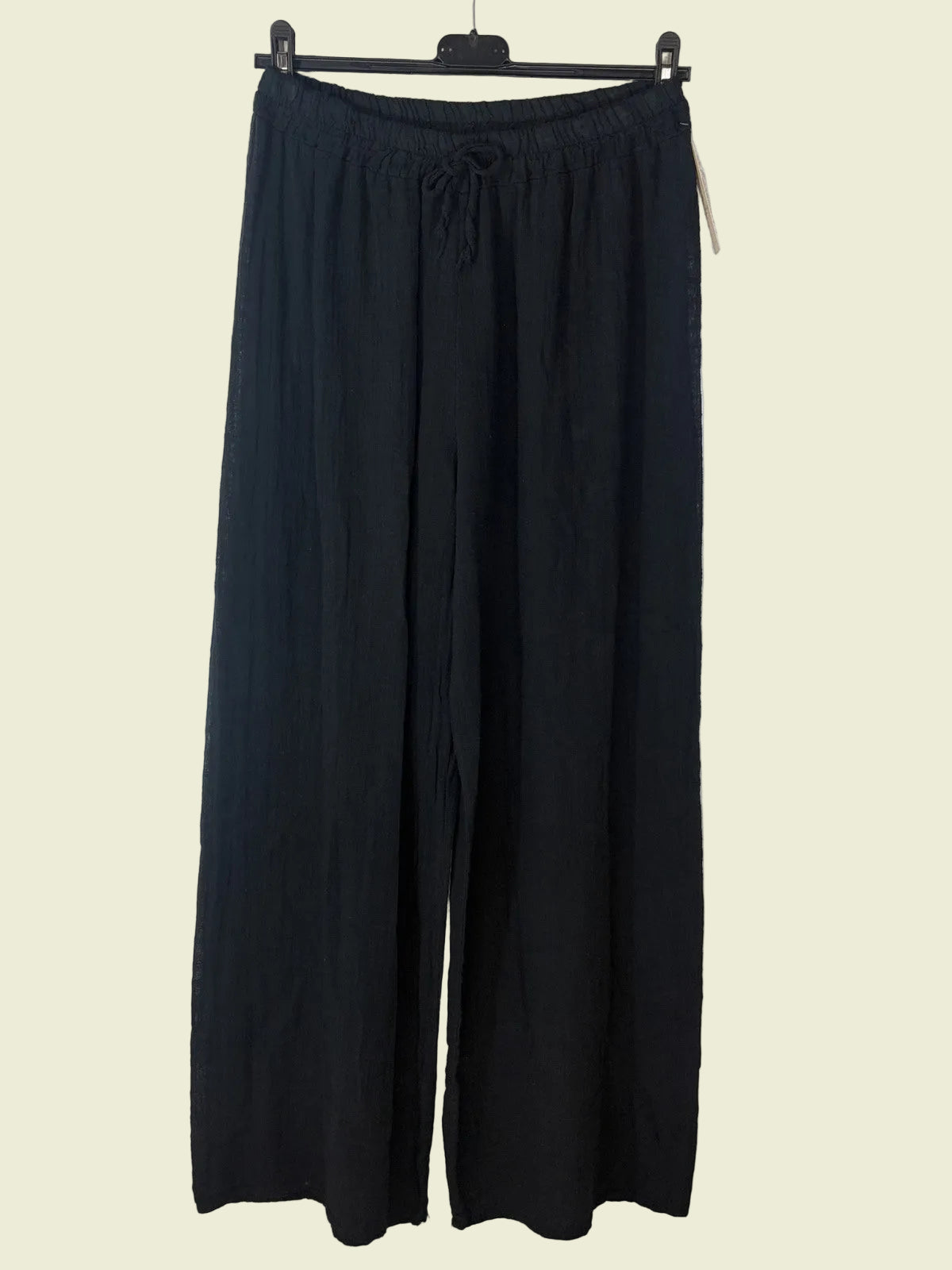 Black wide-leg pants hanging on a rack against a beige wall.