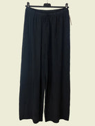Black wide-leg pants hanging on a rack against a beige wall.