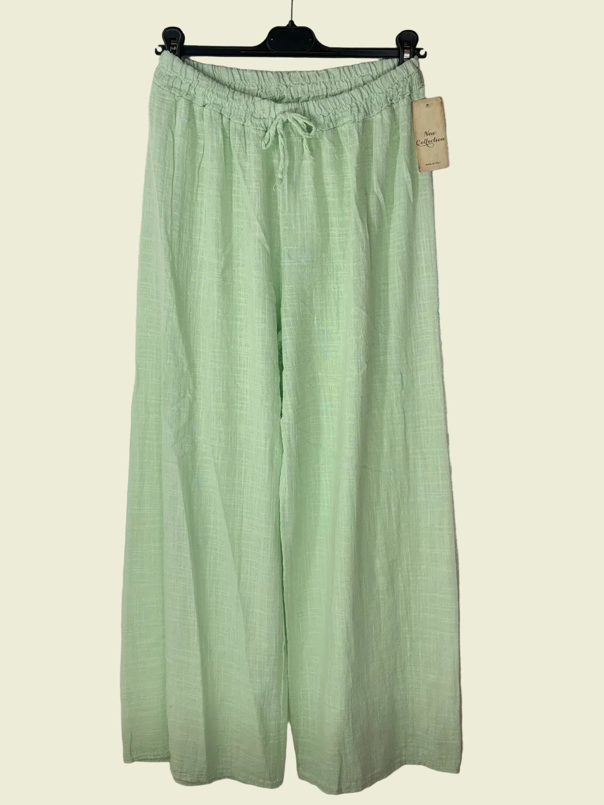 Light green pants on a hanger against a textured gray background