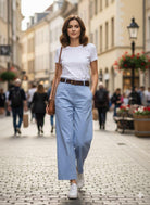 Woman walking down a street wearing a white t-shirt, blue pants, and white sneakers.