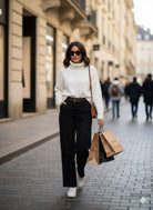 Woman in a white sweater and black pants walking on a city street.