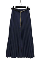 Navy blue pleated skirt with a gold zipper on a hanger against a stone wall background