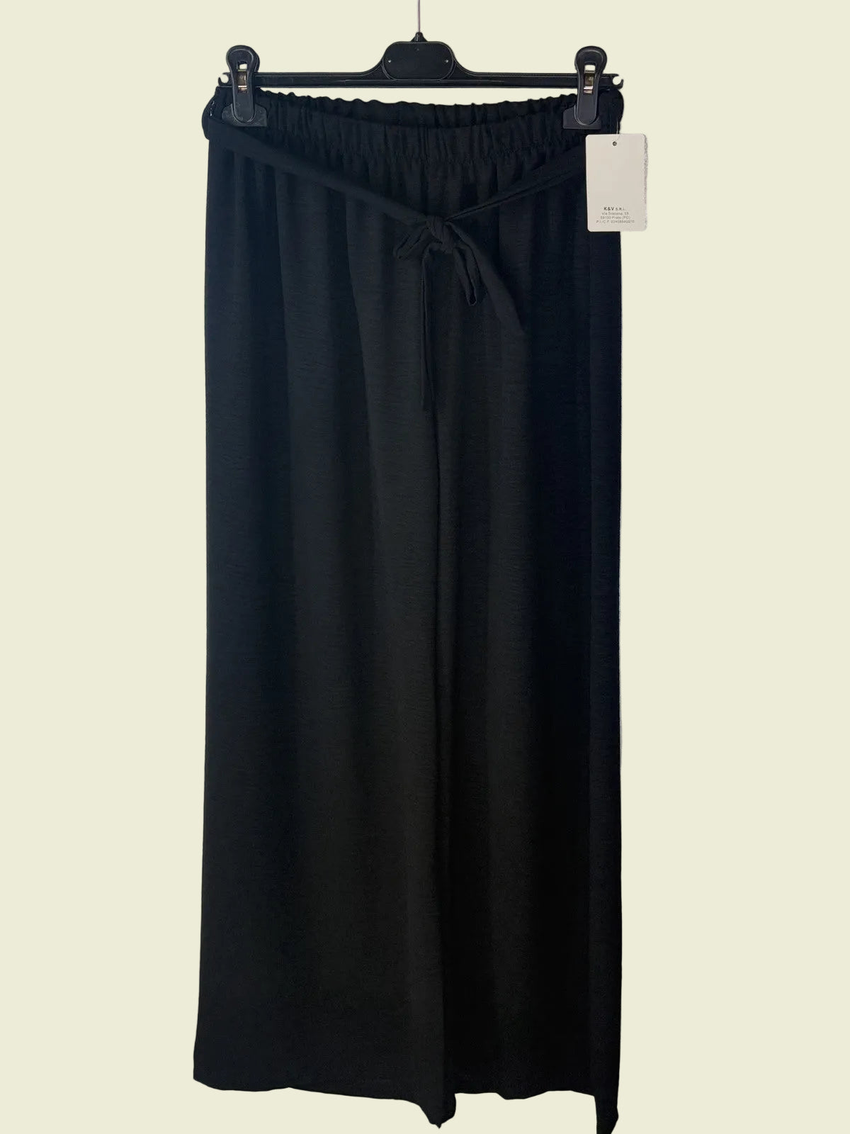 Black pants on a hanger against a textured white background