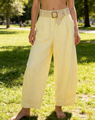 Person wearing light yellow wide-leg pants with a belt in a park setting