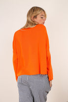 Woman wearing an orange sweater and striped pants against a plain background